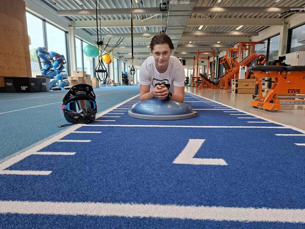 Motorcrosser Dean Gregoire houdt een plankoefening op een bosubal in een sportschool in Eindhoven, met zijn crosshelm naast zich.