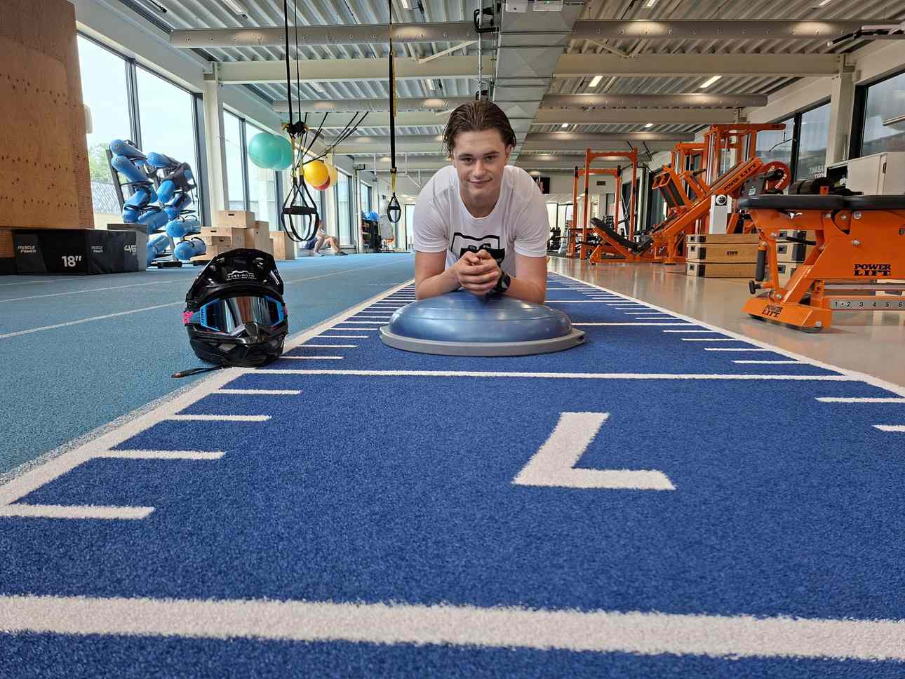 Motorcrosser Dean Gregoire houdt een plankoefening op een bosubal in een sportschool in Eindhoven, met zijn crosshelm naast zich.